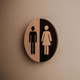 Rundes Holzschild mit Piktogrammen für Herren- und Damentoilette an einer Wand.