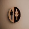 Rundes Holzschild mit Piktogrammen für Herren- und Damentoilette an einer Wand.