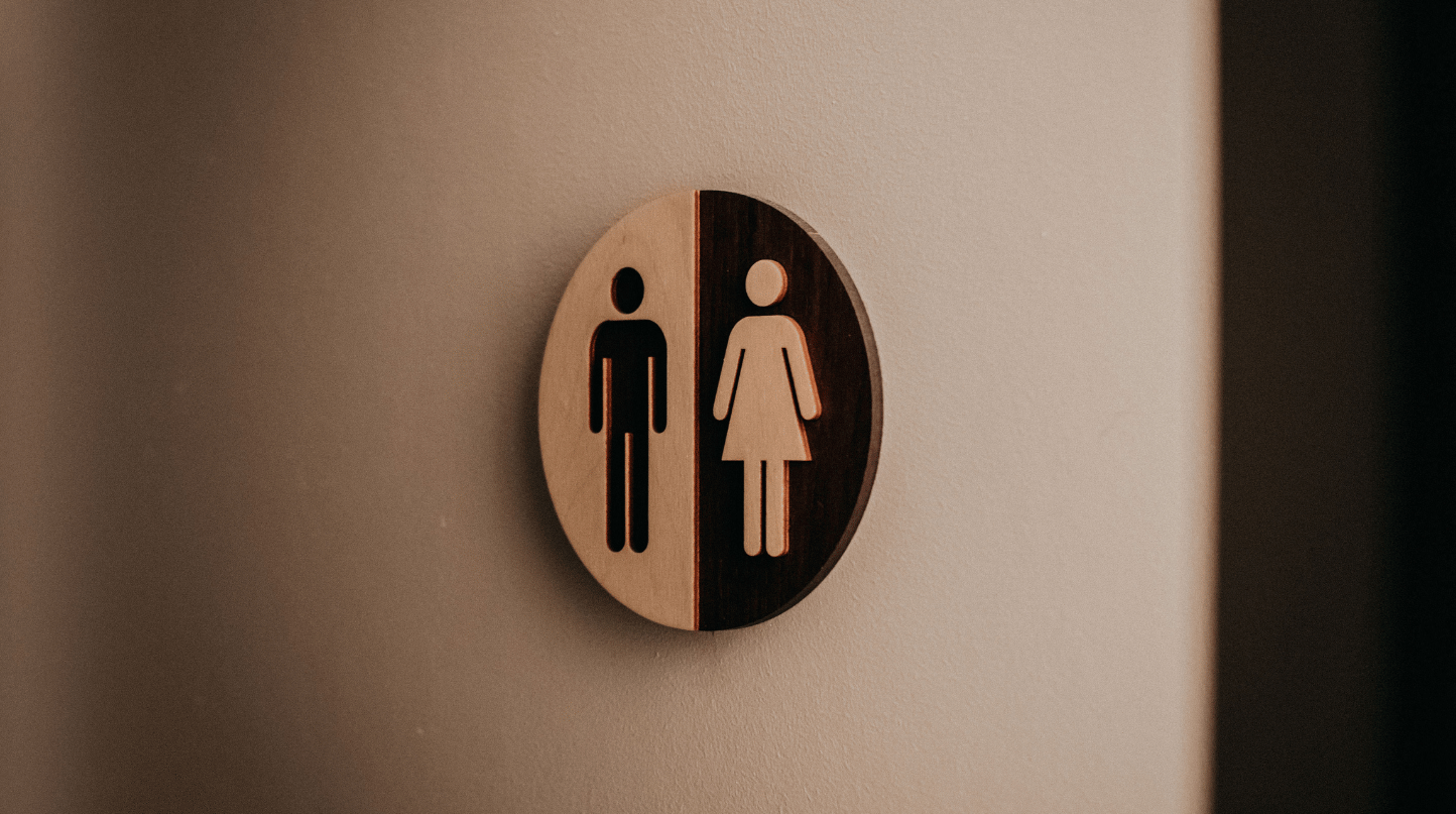 Rundes Holzschild mit Piktogrammen für Herren- und Damentoilette an einer Wand