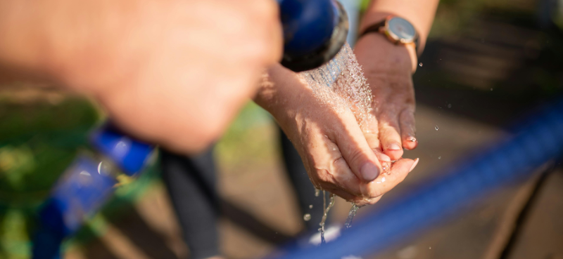Eine Person wäscht sich die Hände mit Wasser aus dem Gartenschlauch